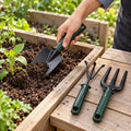 Garden trowel digging soil in a raised bed with hand rake and fork