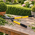 Yellow telescopic hedge shears on a garden table beside trimmed hedge clippings